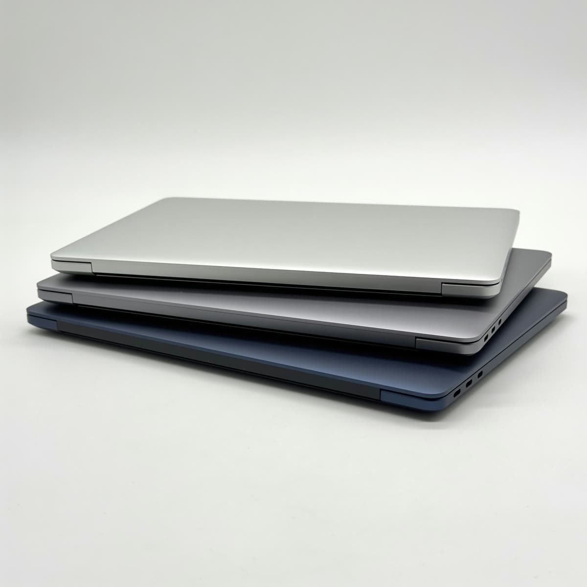 Drei geschlossene Notebooks in Silber, Grau und Mitternachtsblau, gestaffelt übereinander